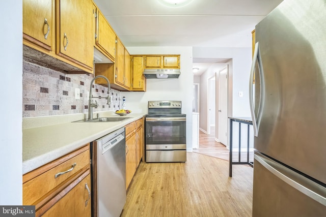 kitchen featuring light countertops, under cabinet range hood, a sink, light wood finished floors, and appliances with stainless steel finishes