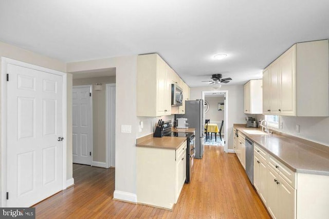kitchen with light wood-style flooring, a ceiling fan, appliances with stainless steel finishes, a sink, and baseboards