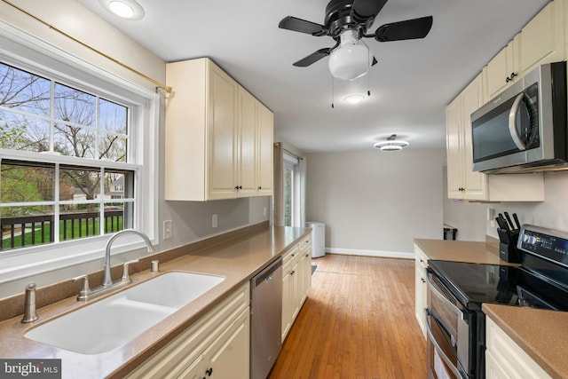 kitchen featuring ceiling fan, light wood-style flooring, a sink, stainless steel appliances, and baseboards