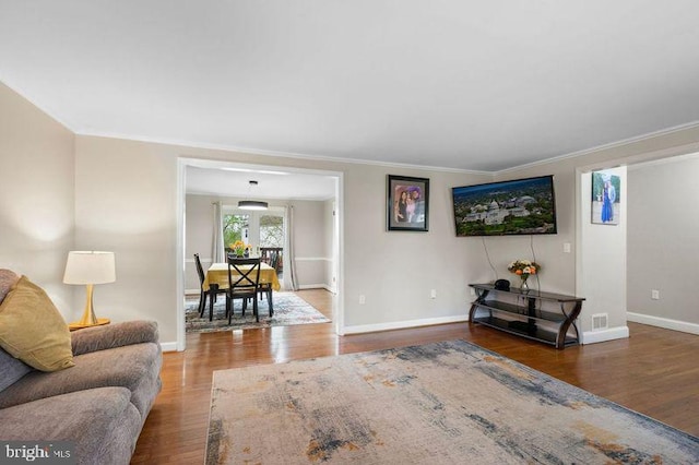 living area with crown molding, visible vents, baseboards, and wood finished floors
