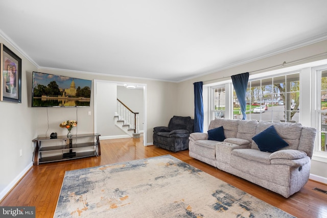 living area featuring ornamental molding, baseboards, wood finished floors, and stairs