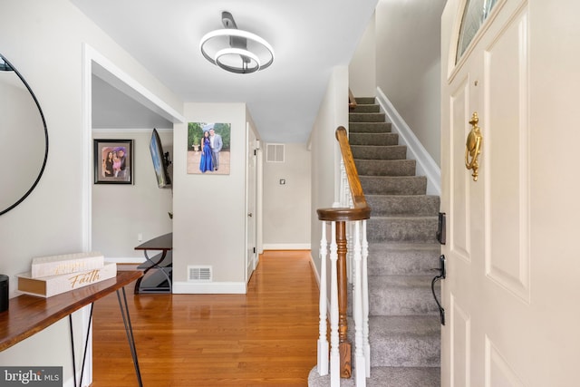foyer entrance with visible vents, baseboards, light wood-type flooring, and stairway