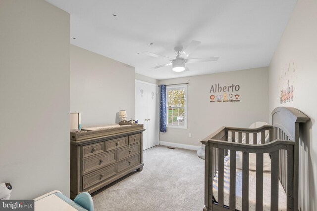 bedroom featuring baseboards, a crib, visible vents, ceiling fan, and light colored carpet