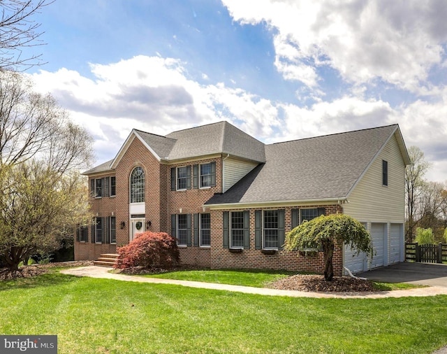 colonial inspired home with brick siding, an attached garage, driveway, and a front yard