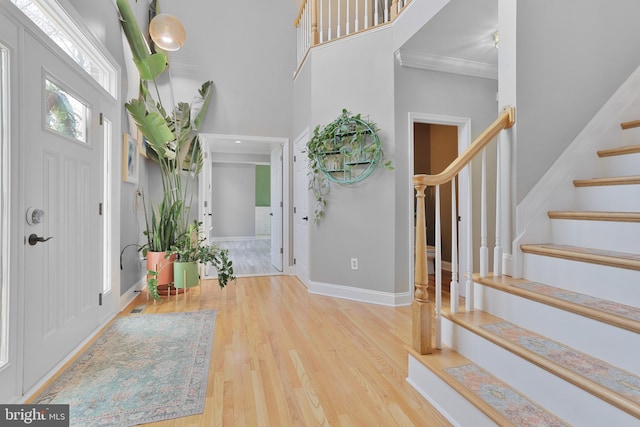 foyer featuring stairs, wood finished floors, baseboards, a high ceiling, and ornamental molding