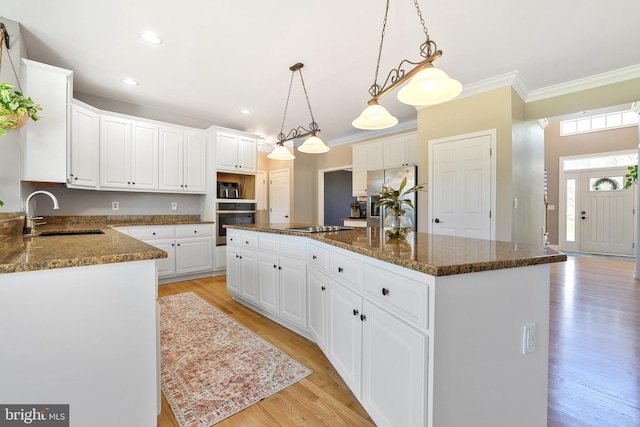 kitchen with crown molding, a sink, light wood-style floors, stainless steel appliances, and a kitchen island