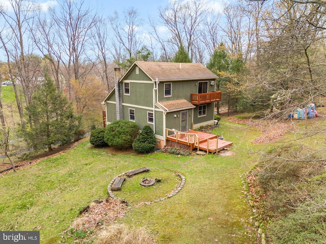 rear view of property featuring a lawn, an outdoor fire pit, a balcony, a chimney, and a deck