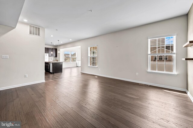 unfurnished living room featuring visible vents, recessed lighting, a sink, baseboards, and dark wood-style floors
