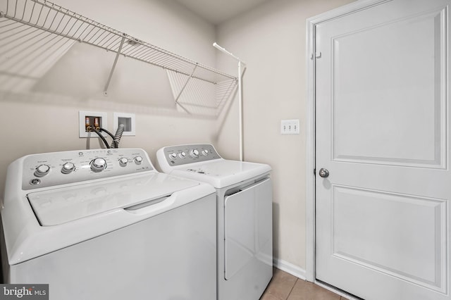 clothes washing area with washer and dryer, laundry area, light tile patterned floors, and baseboards