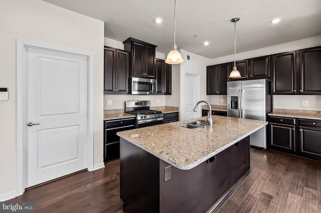 kitchen with a sink, appliances with stainless steel finishes, light stone countertops, dark wood-type flooring, and pendant lighting