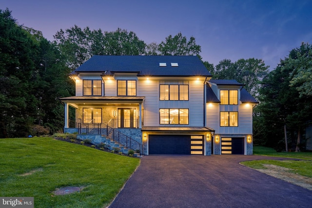 contemporary house featuring stairs, an attached garage, driveway, covered porch, and a front yard