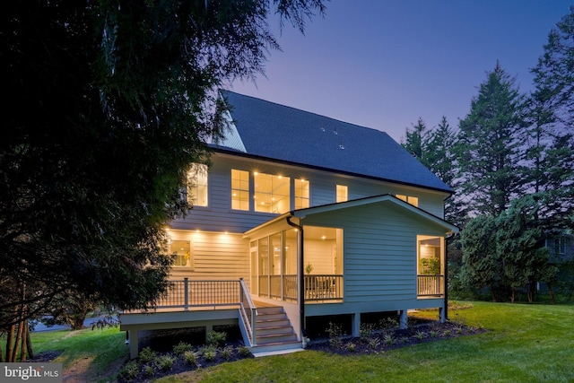 back of house at dusk featuring a deck, stairway, a yard, and a shingled roof