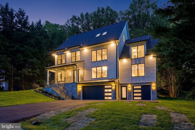 contemporary home with a standing seam roof, concrete driveway, an attached garage, stairs, and a front yard