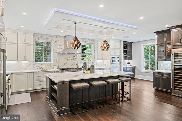 kitchen with wall chimney exhaust hood, stainless steel appliances, backsplash, and a raised ceiling