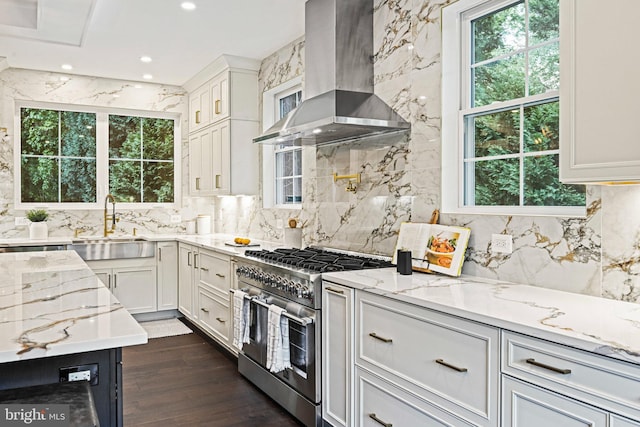 kitchen featuring wall chimney range hood, light stone counters, decorative backsplash, high end range, and white cabinetry