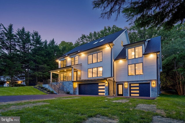 contemporary house featuring stairway, an attached garage, driveway, stone siding, and a front yard