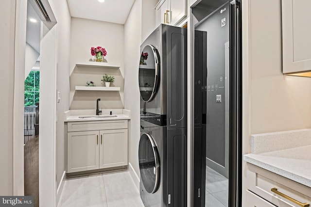 washroom with stacked washer and dryer, baseboards, a sink, and light tile patterned flooring