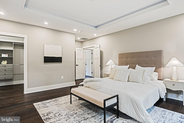 bedroom with recessed lighting, dark wood finished floors, a walk in closet, and a tray ceiling