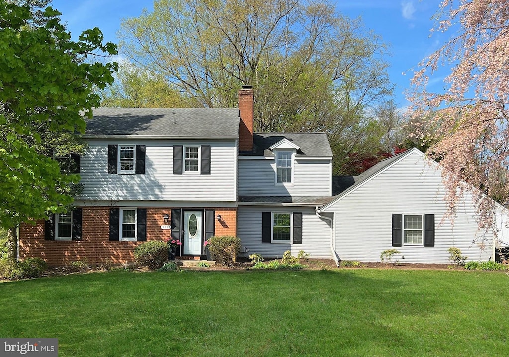 view of front of house featuring brick siding, a front lawn, and a chimney