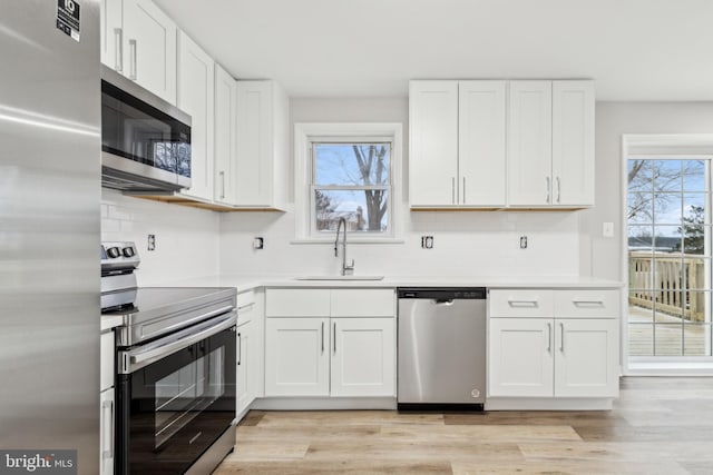 kitchen with light countertops, a sink, white cabinetry, light wood-style flooring, and stainless steel appliances