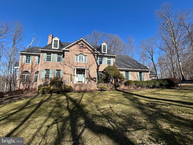 georgian-style home featuring a chimney, a front yard, and brick siding