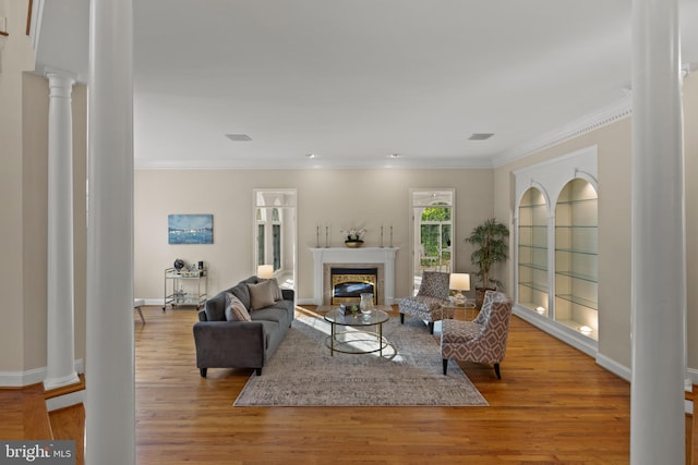 living room with a glass covered fireplace, baseboards, decorative columns, wood finished floors, and ornamental molding