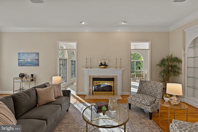 living area with a fireplace with flush hearth, baseboards, ornamental molding, and wood finished floors