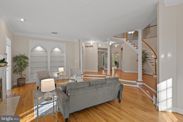 living area with crown molding, light wood-style floors, stairs, ornate columns, and visible vents