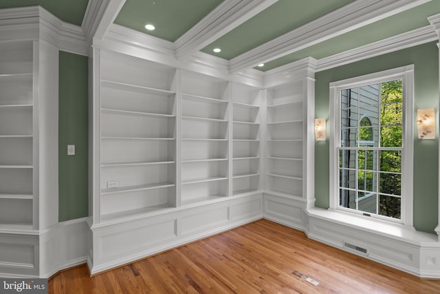 unfurnished room featuring crown molding, built in features, wood finished floors, and visible vents