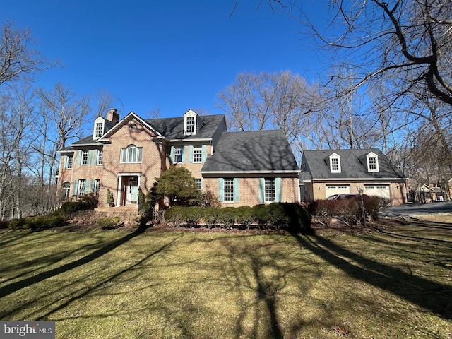 view of front of house featuring brick siding, driveway, a chimney, and a front lawn