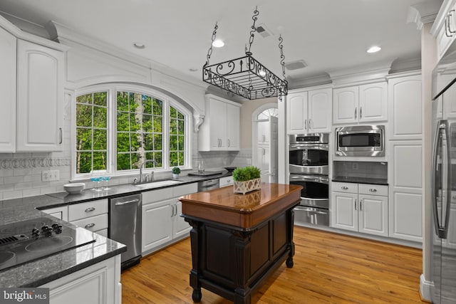 kitchen with appliances with stainless steel finishes, tasteful backsplash, arched walkways, a sink, and white cabinetry