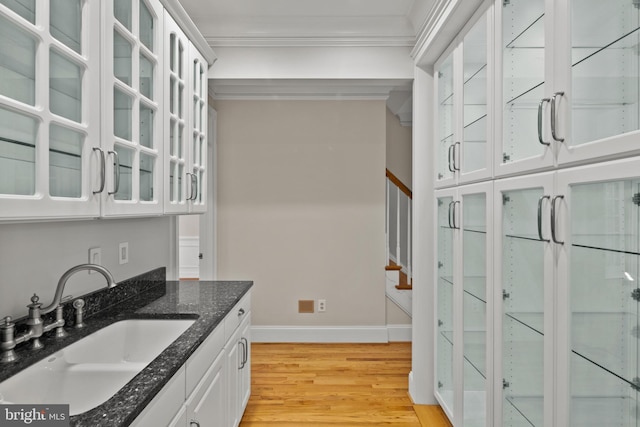 bar with crown molding, a sink, baseboards, light wood-style floors, and stairs