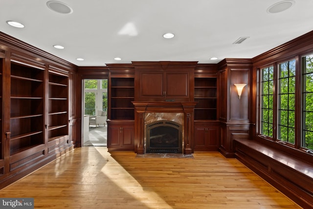 unfurnished living room featuring a healthy amount of sunlight, a premium fireplace, light wood finished floors, and visible vents