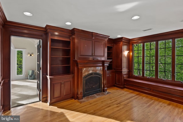 unfurnished living room featuring visible vents, ornamental molding, light wood-style floors, and a premium fireplace