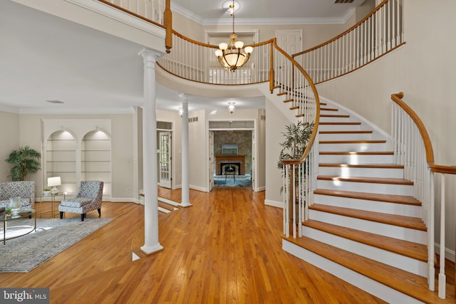 foyer entrance featuring ornamental molding, decorative columns, wood finished floors, a stone fireplace, and stairway
