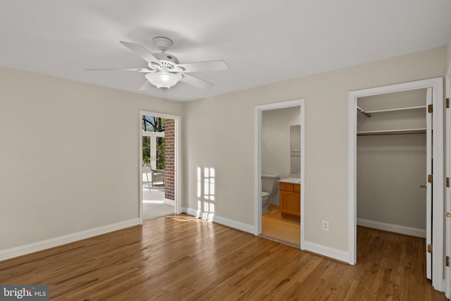 unfurnished bedroom with a walk in closet, baseboards, a closet, light wood finished floors, and connected bathroom