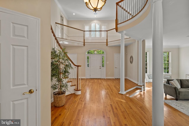 entrance foyer featuring stairway, baseboards, ornate columns, ornamental molding, and hardwood / wood-style flooring