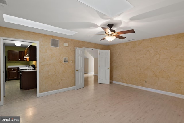 unfurnished room featuring visible vents, a ceiling fan, a skylight, and light wood-type flooring
