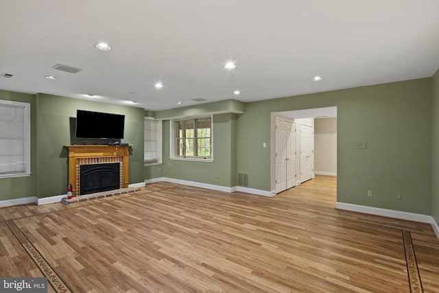 unfurnished living room featuring recessed lighting, baseboards, a brick fireplace, and light wood finished floors