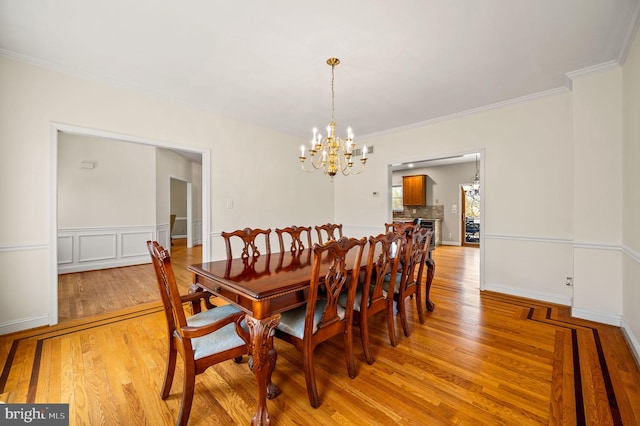 dining area with ornamental molding, light wood finished floors, and a notable chandelier
