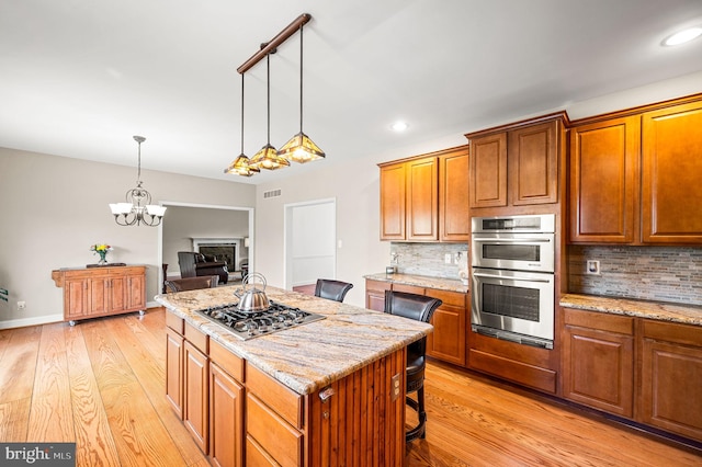 kitchen featuring light wood-style flooring, backsplash, an inviting chandelier, and appliances with stainless steel finishes