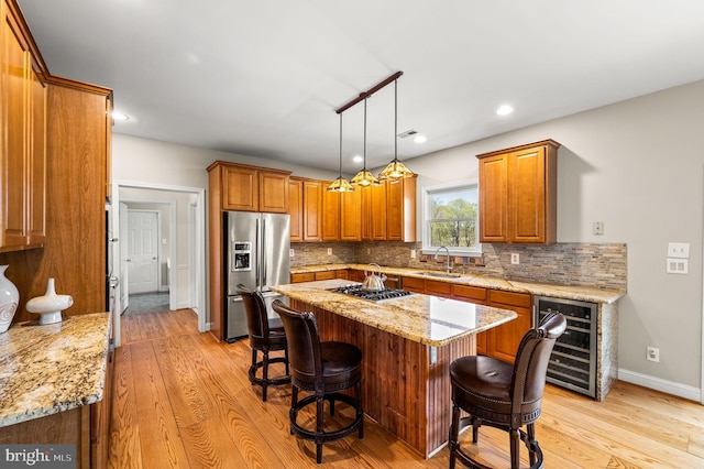kitchen featuring a sink, wine cooler, light wood-style flooring, backsplash, and appliances with stainless steel finishes