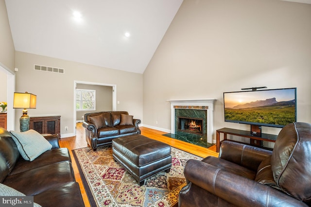 living area featuring high vaulted ceiling, visible vents, baseboards, a high end fireplace, and wood finished floors