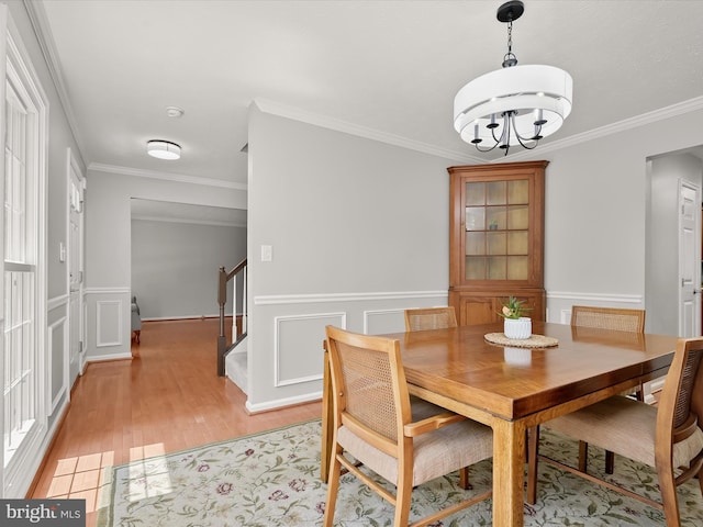 dining room with stairway, a chandelier, light wood-style floors, ornamental molding, and a wainscoted wall