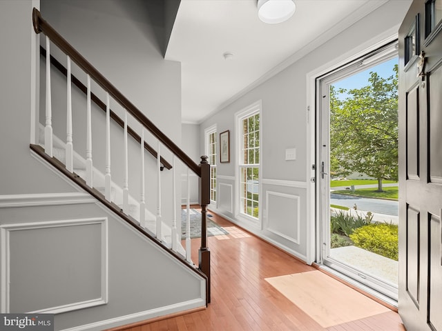 foyer with ornamental molding, stairs, light wood-style floors, and a decorative wall