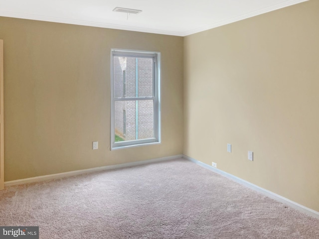 carpeted spare room featuring plenty of natural light, crown molding, baseboards, and visible vents