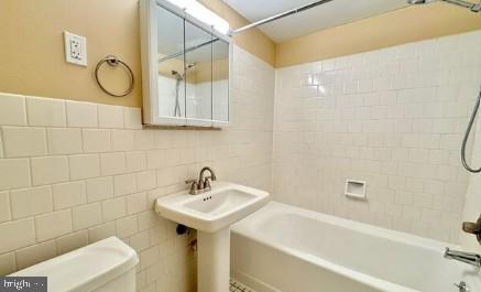bathroom with toilet, a sink, shower / bath combination, and tile walls