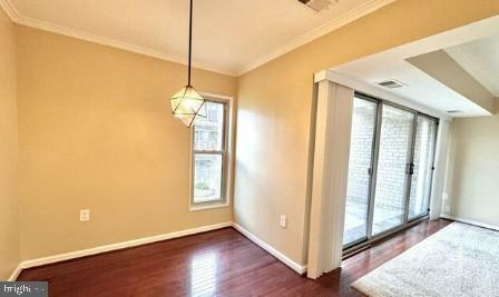 unfurnished dining area featuring dark wood finished floors, baseboards, visible vents, and ornamental molding