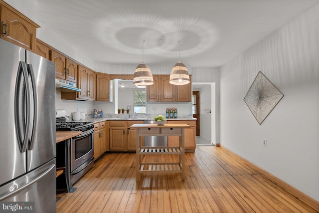 kitchen with stainless steel appliances, light countertops, light wood-type flooring, under cabinet range hood, and a sink