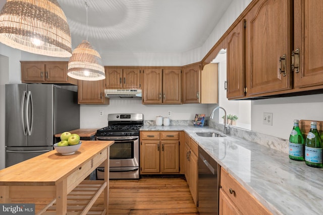 kitchen featuring stainless steel appliances, a sink, under cabinet range hood, light wood finished floors, and light stone countertops